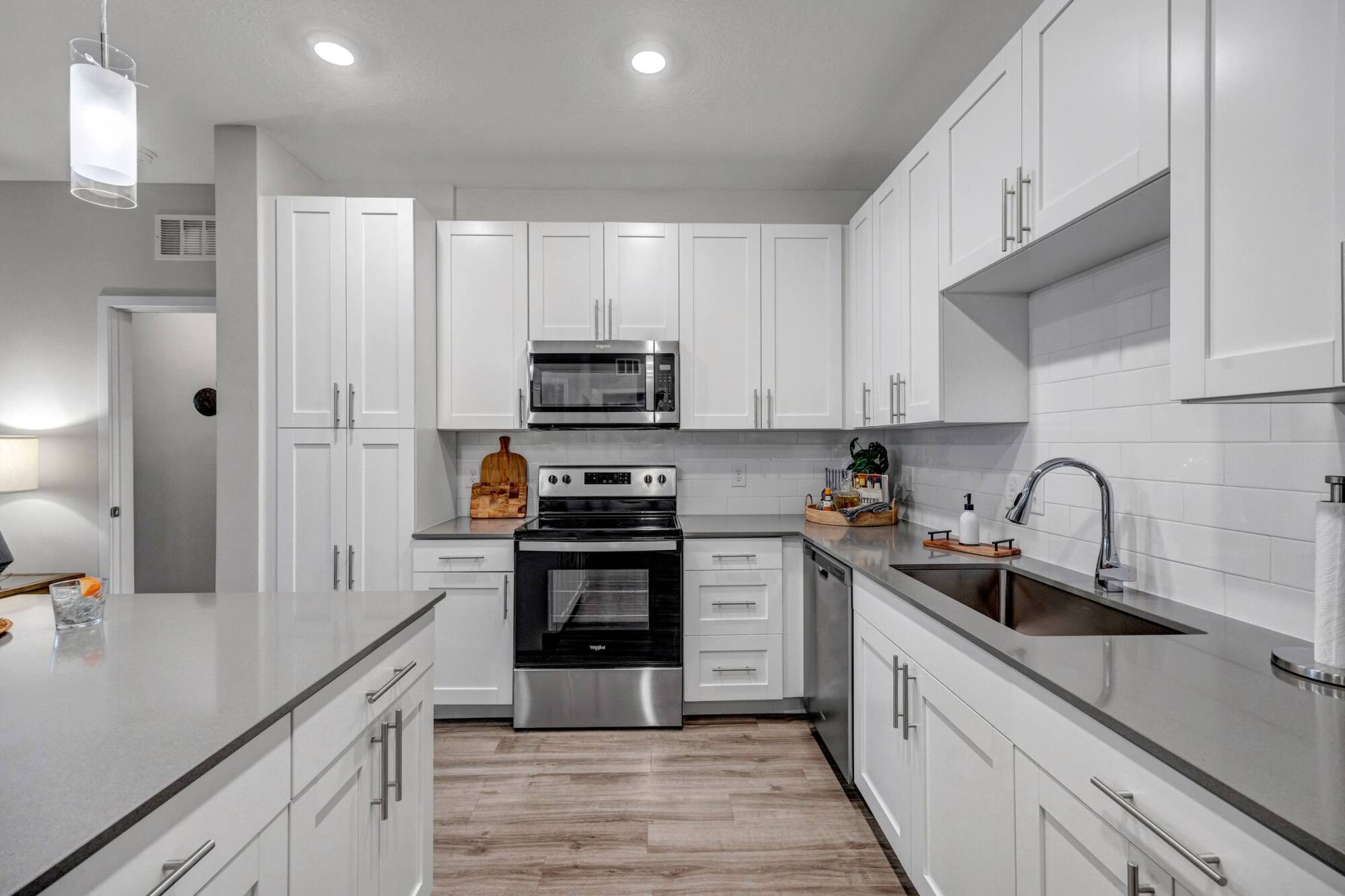 Modern kitchen with white cabinets, stainless steel appliances, and gray countertops under bright lighting.